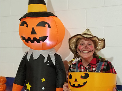 lady dressed as scarecrow standing next to jack o lantern