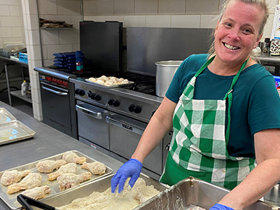 Lady wearing apron in the school kitchen preparing chicken dish