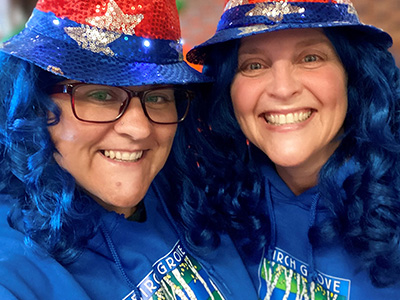 Two ladies wearing red and blue hats, blue hair, and Birch Grove shirts